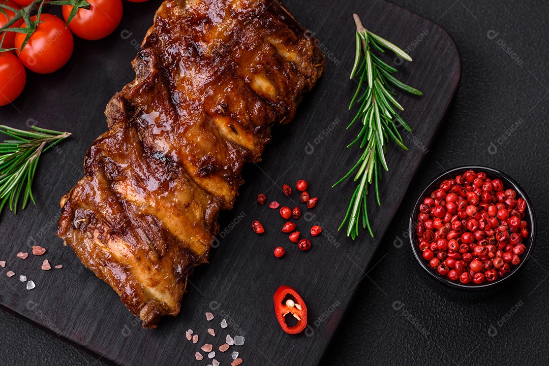 Deliciosas costelas de porco grelhadas com molho, especiarias e ervas sobre um fundo escuro de concreto