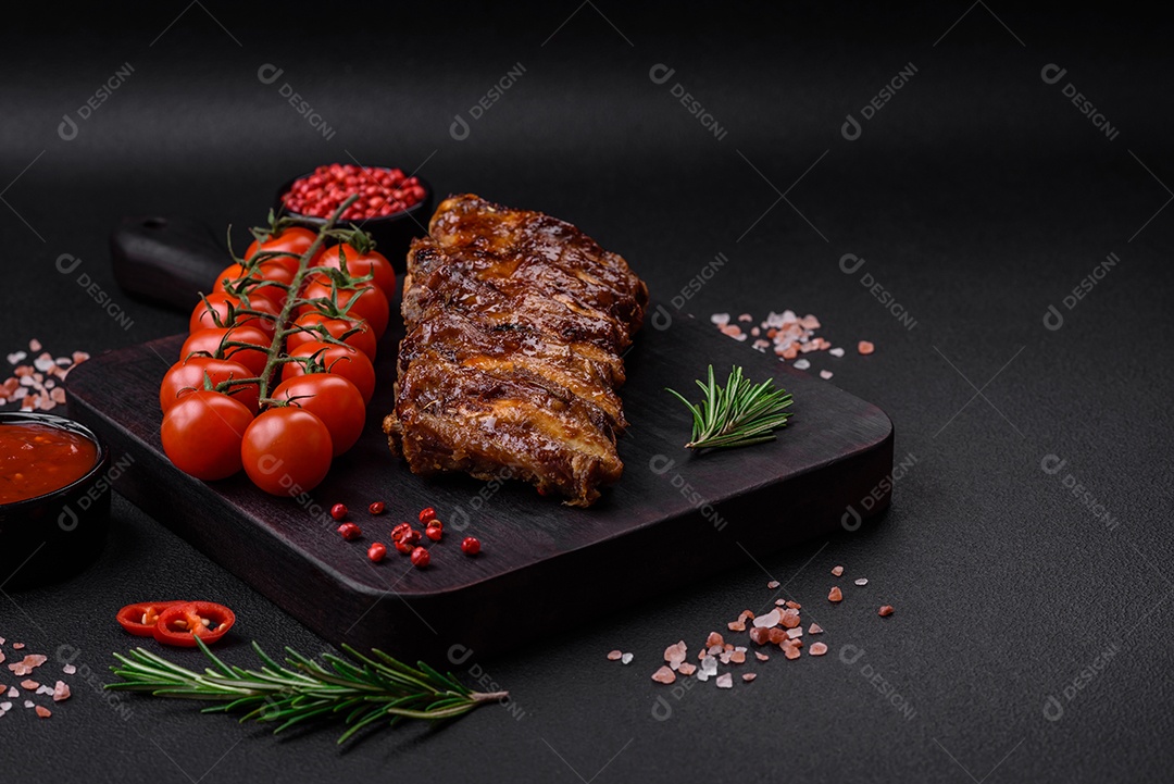 Deliciosas costelas de porco grelhadas com molho, especiarias e ervas sobre um fundo escuro de concreto