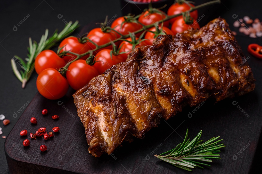 Deliciosas costelas de porco grelhadas com molho, especiarias e ervas sobre um fundo escuro de concreto