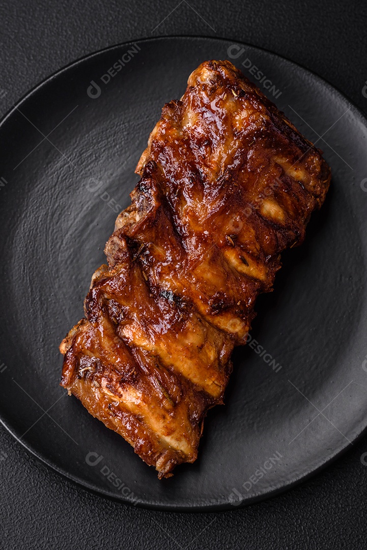 Deliciosas costelas de porco grelhadas com molho, especiarias e ervas sobre um fundo escuro de concreto