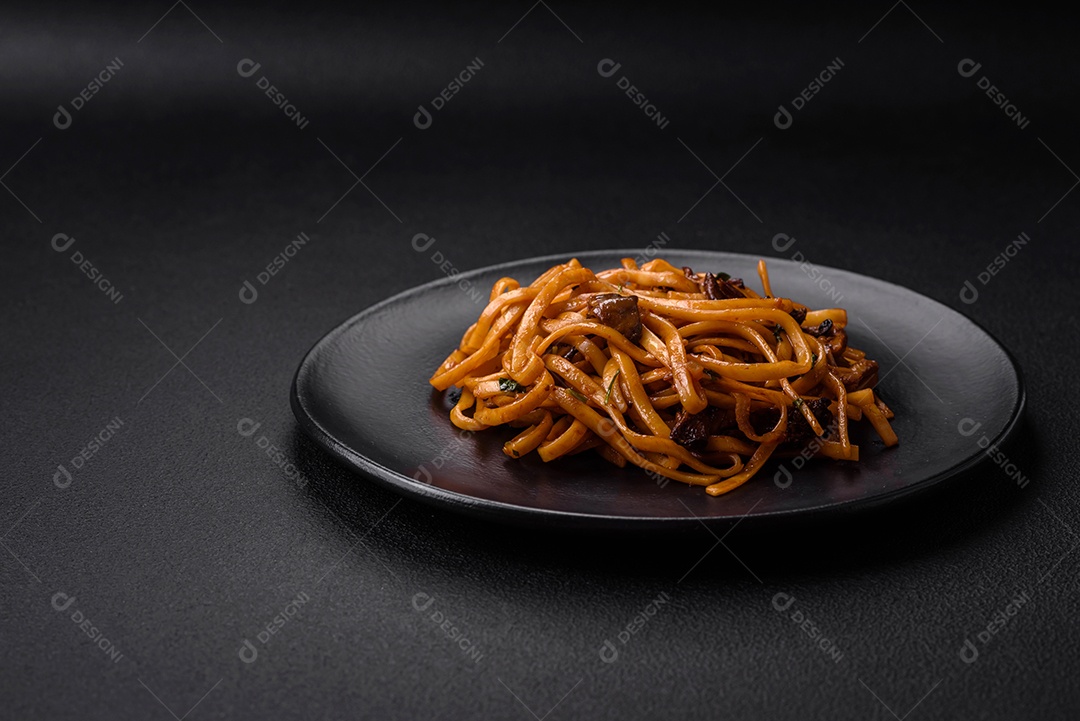 Delicioso macarrão ou udon com cogumelos, sal, especiarias e ervas em uma placa cerâmica sobre um fundo escuro de concreto
