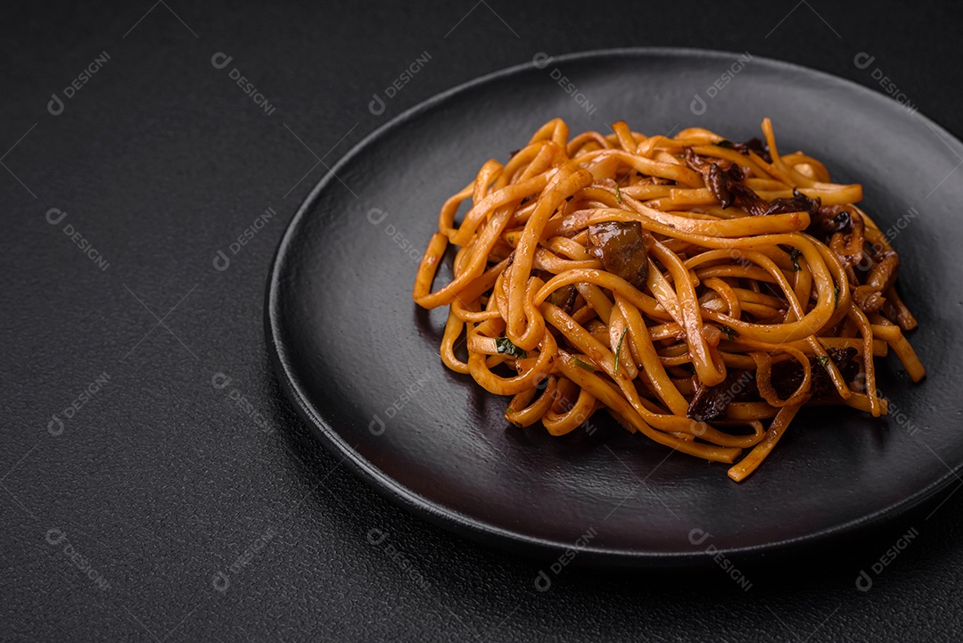 Delicioso macarrão ou udon com cogumelos, sal, especiarias e ervas em uma placa cerâmica sobre um fundo escuro de concreto