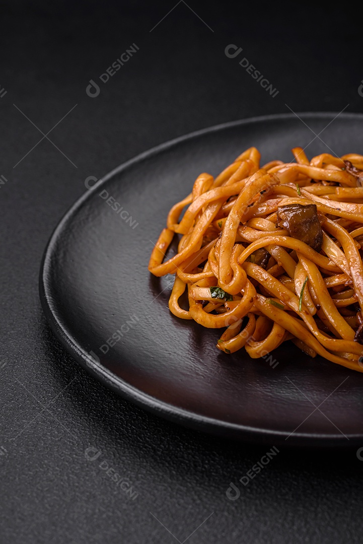 Delicioso macarrão ou udon com cogumelos, sal, especiarias e ervas em uma placa cerâmica sobre um fundo escuro de concreto