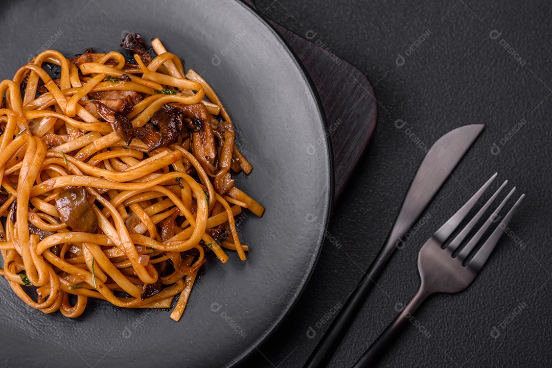 Delicioso macarrão ou udon com cogumelos, sal, especiarias e ervas em uma placa cerâmica sobre um fundo escuro de concreto