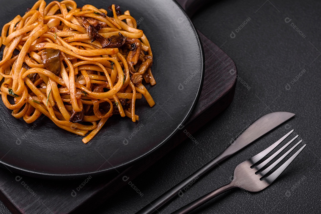 Delicioso macarrão ou udon com cogumelos, sal, especiarias e ervas em uma placa cerâmica sobre um fundo escuro de concreto