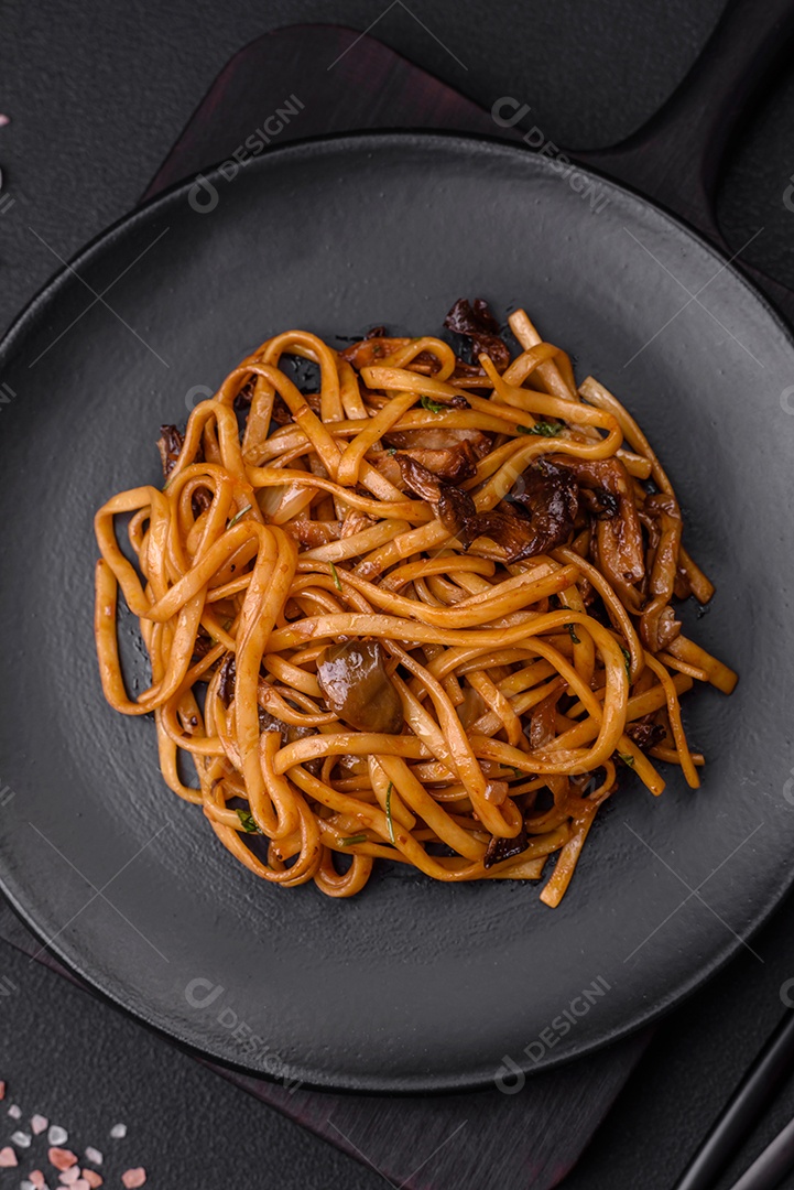 Delicioso macarrão ou udon com cogumelos, sal, especiarias e ervas em uma placa cerâmica sobre um fundo escuro de concreto