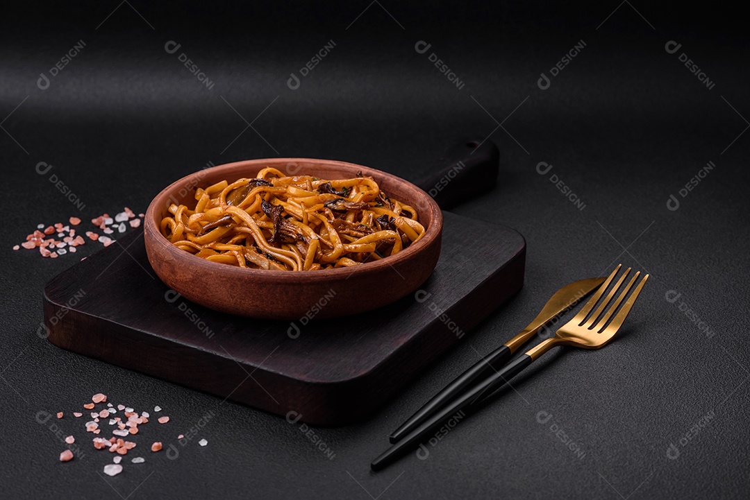 Delicioso macarrão ou udon com cogumelos, sal, especiarias e ervas em uma placa cerâmica sobre um fundo escuro de concreto