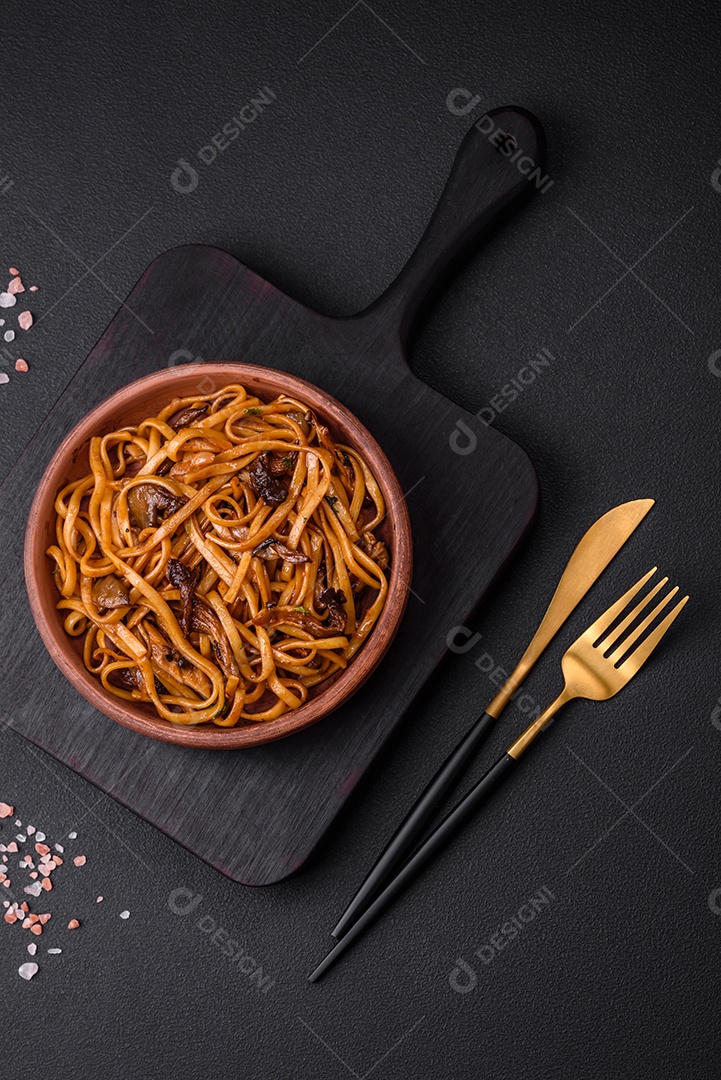 Delicioso macarrão ou udon com cogumelos, sal, especiarias e ervas em uma placa cerâmica sobre um fundo escuro de concreto