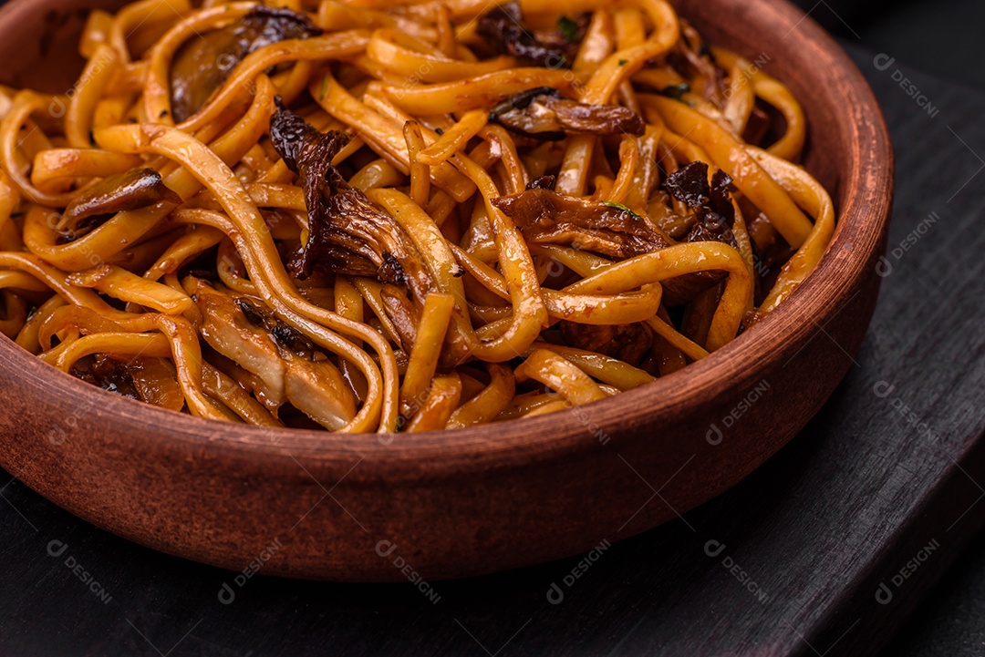 Delicioso macarrão ou udon com cogumelos, sal, especiarias e ervas em uma placa cerâmica sobre um fundo escuro de concreto