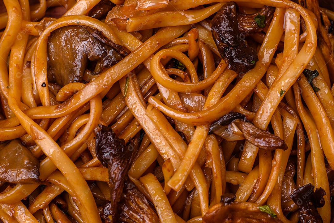 Delicioso macarrão ou udon com cogumelos, sal, especiarias e ervas em uma placa cerâmica sobre um fundo escuro de concreto