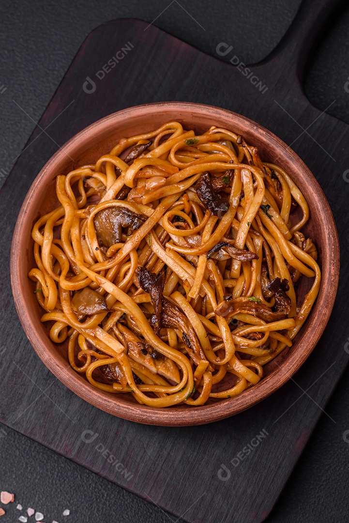 Delicioso macarrão ou udon com cogumelos, sal, especiarias e ervas em uma placa cerâmica sobre um fundo escuro de concreto