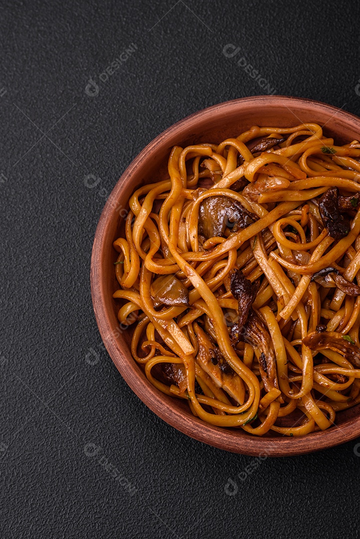 Delicioso macarrão ou udon com cogumelos, sal, especiarias e ervas em uma placa cerâmica sobre um fundo escuro de concreto