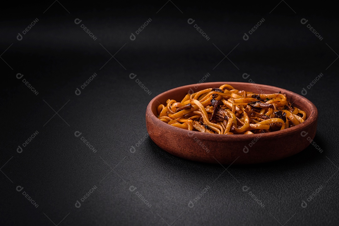 Delicioso macarrão ou udon com cogumelos, sal, especiarias e ervas em uma placa cerâmica sobre um fundo escuro de concreto