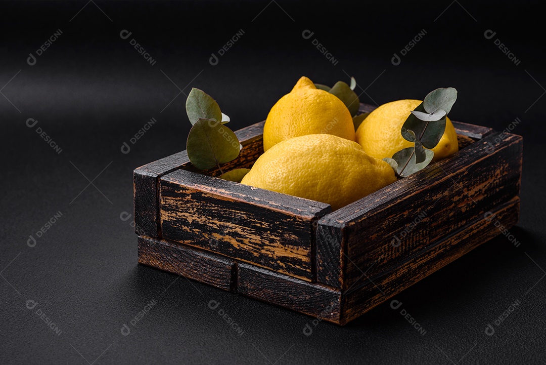 Deliciosas frutas cítricas amarelas frescas ou limão em uma caixa de madeira sobre um fundo escuro de concreto