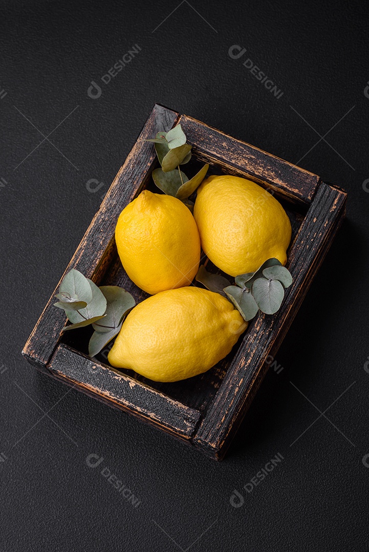 Deliciosas frutas cítricas amarelas frescas ou limão em uma caixa de madeira sobre um fundo escuro de concreto