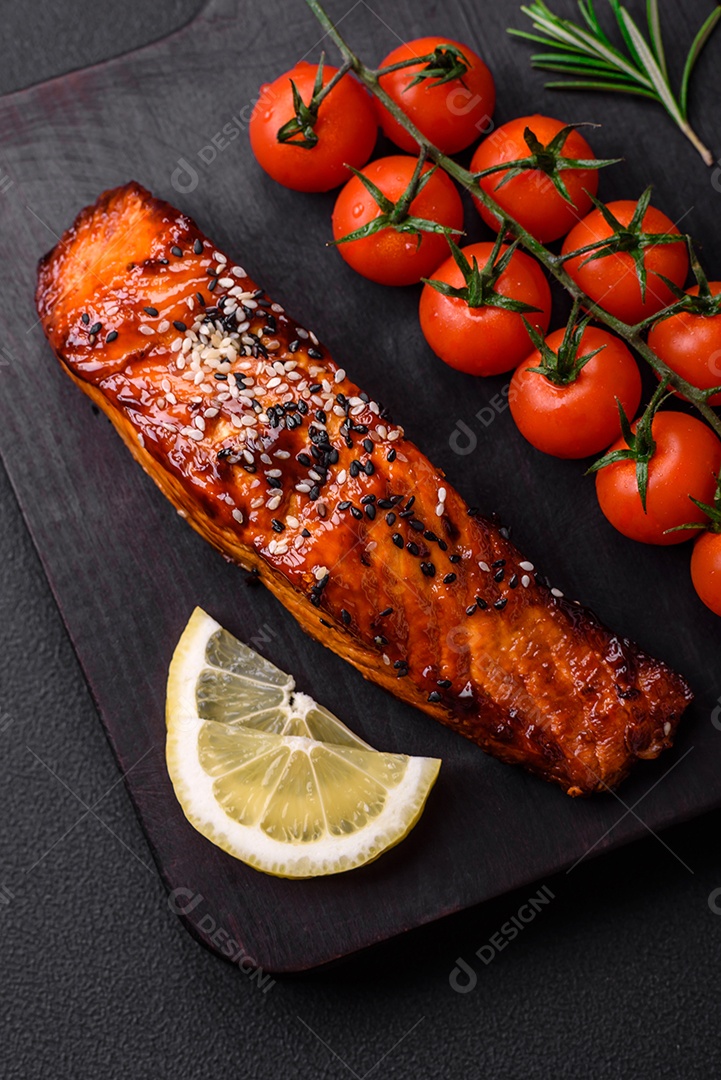 Delicioso salmão vermelho grelhado com molho, sementes de gergelim, especiarias e ervas sobre fundo escuro de concreto