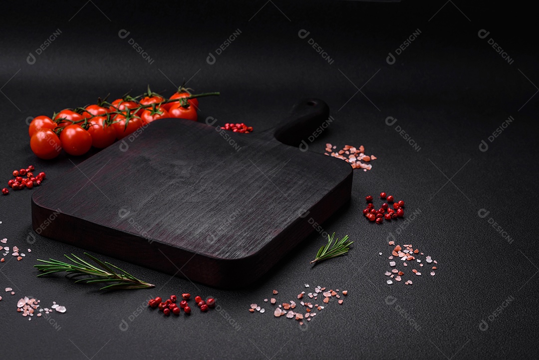 Tábua de corte de madeira vazia com tomate cereja, especiarias, sal e ervas em fundo escuro de concreto