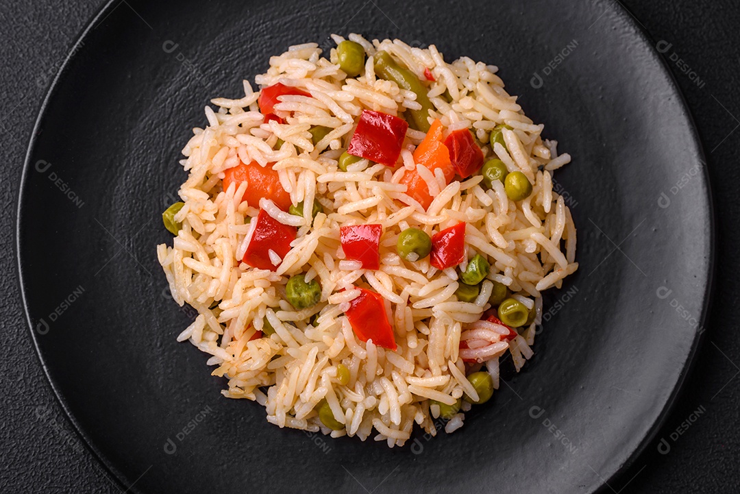 Delicioso arroz cozido com legumes, pimentões, cenouras, ervilhas e feijões de espargos com especiarias e ervas sobre um fundo escuro de concreto