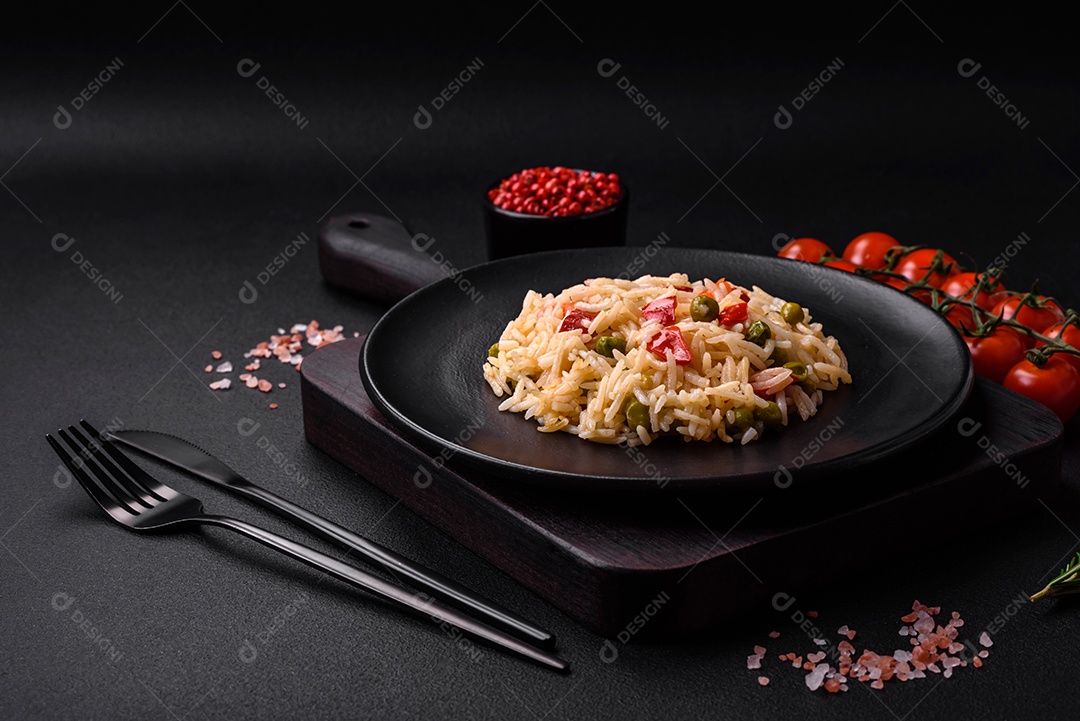 Delicioso arroz cozido com legumes, pimentões, cenouras, ervilhas e feijões de espargos com especiarias e ervas sobre um fundo escuro de concreto