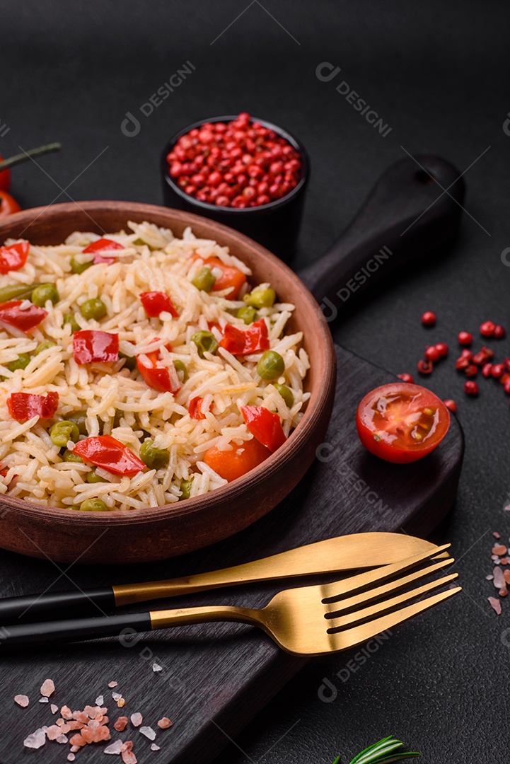 Delicioso arroz cozido com legumes, pimentões, cenouras, ervilhas e feijões de espargos com especiarias e ervas sobre um fundo escuro de concreto