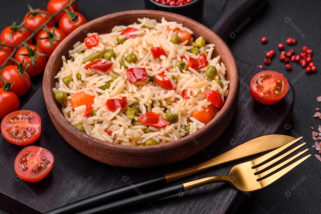 Delicioso arroz cozido com legumes, pimentões, cenouras, ervilhas e feijões de espargos com especiarias e ervas sobre um fundo escuro de concreto