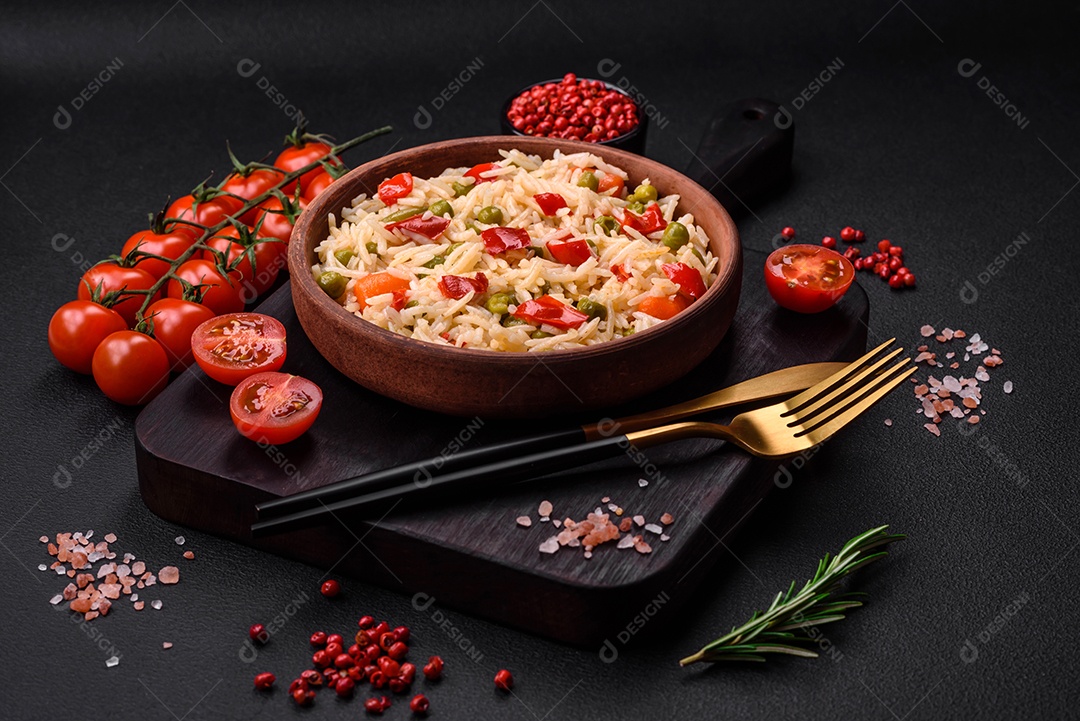 Delicioso arroz cozido com legumes, pimentões, cenouras, ervilhas e feijões de espargos com especiarias e ervas sobre um fundo escuro de concreto