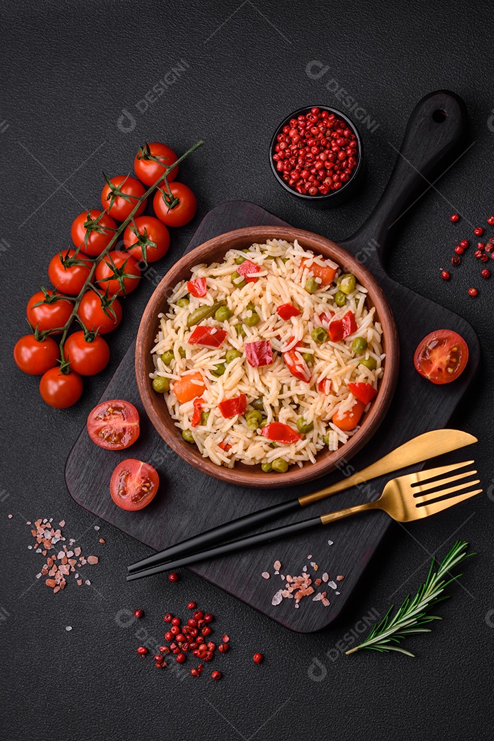 Delicioso arroz cozido com legumes, pimentões, cenouras, ervilhas e feijões de espargos com especiarias e ervas sobre um fundo escuro de concreto