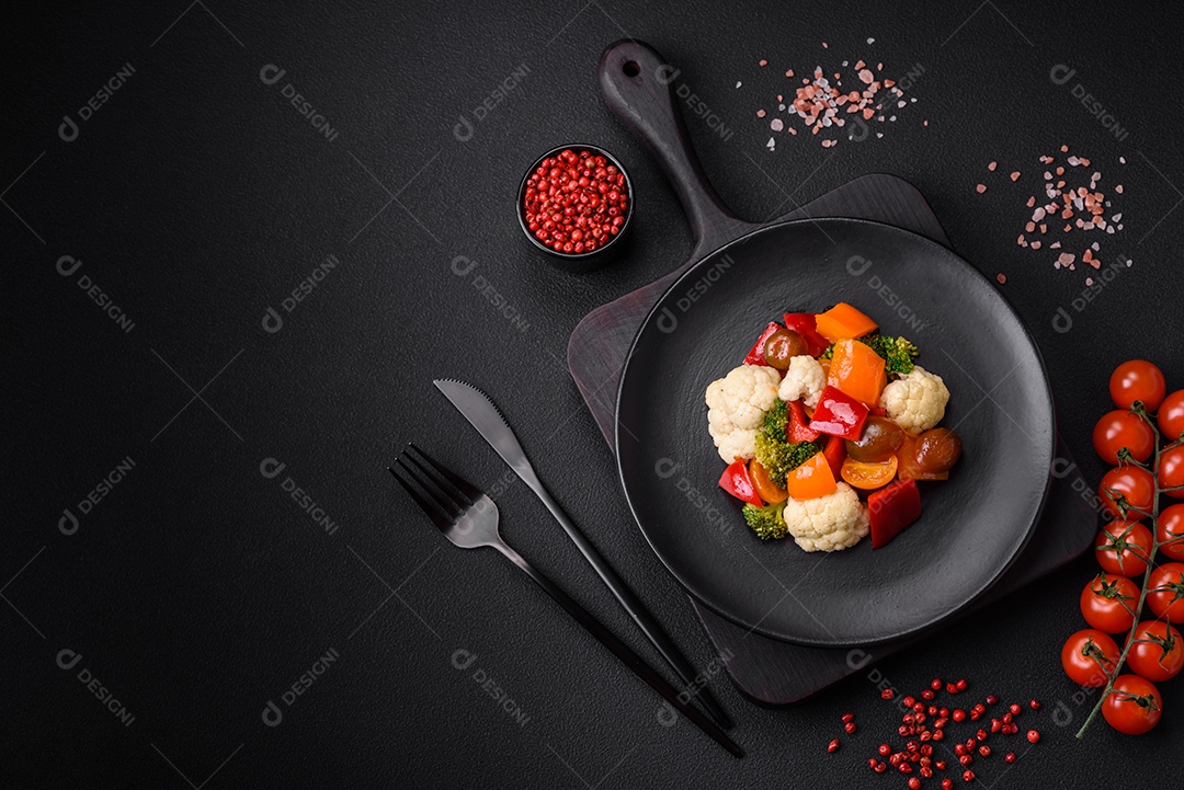 Deliciosa salada de tomate cereja fresco, pimentão, brócolis e couve-flor com sal e especiarias sobre um fundo escuro de concreto