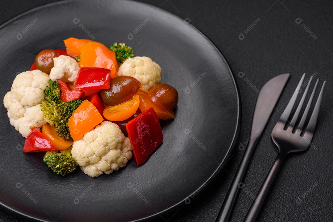 Deliciosa salada de tomate cereja fresco, pimentão, brócolis e couve-flor com sal e especiarias sobre um fundo escuro de concreto