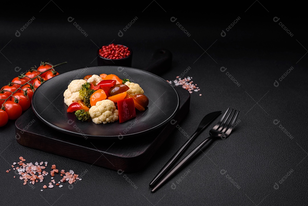 Deliciosa salada de tomate cereja fresco, pimentão, brócolis e couve-flor com sal e especiarias sobre um fundo escuro de concreto