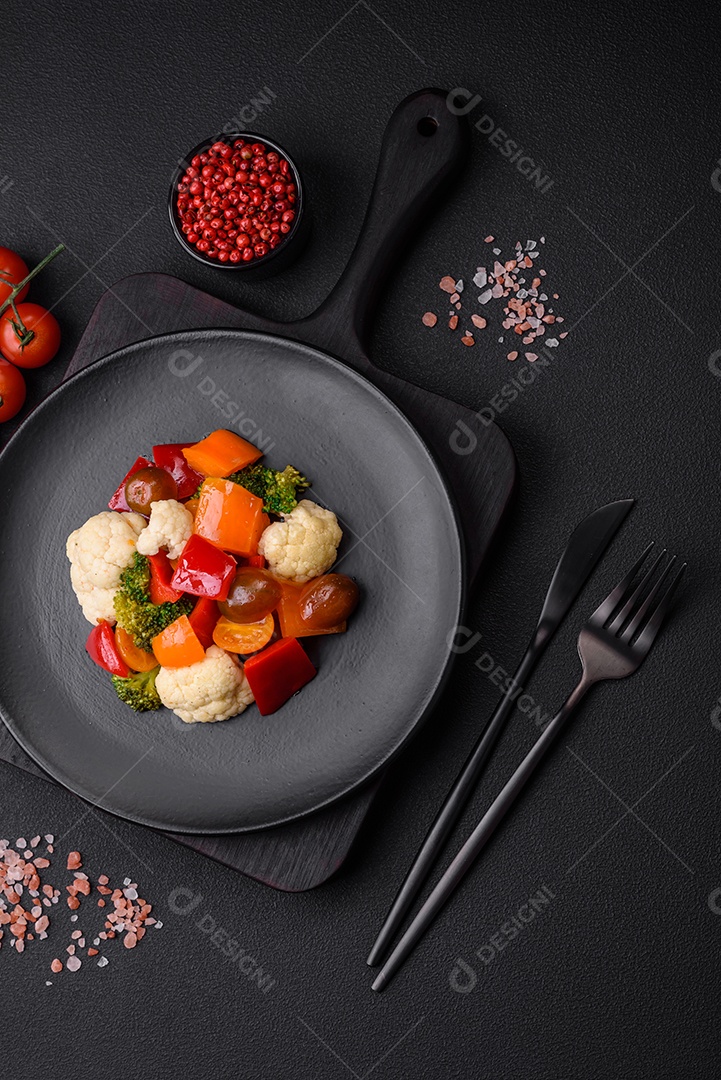Deliciosa salada de tomate cereja fresco, pimentão, brócolis e couve-flor com sal e especiarias sobre um fundo escuro de concreto