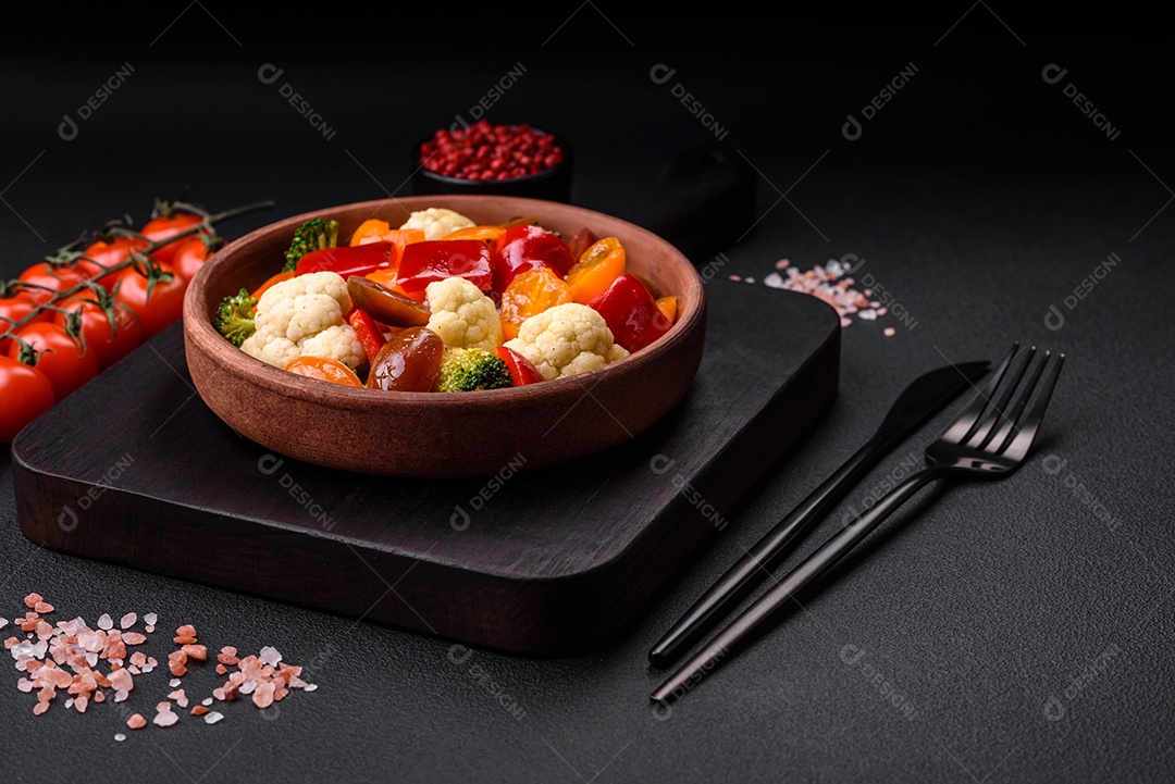 Deliciosa salada de tomate cereja fresco, pimentão, brócolis e couve-flor com sal e especiarias sobre um fundo escuro de concreto