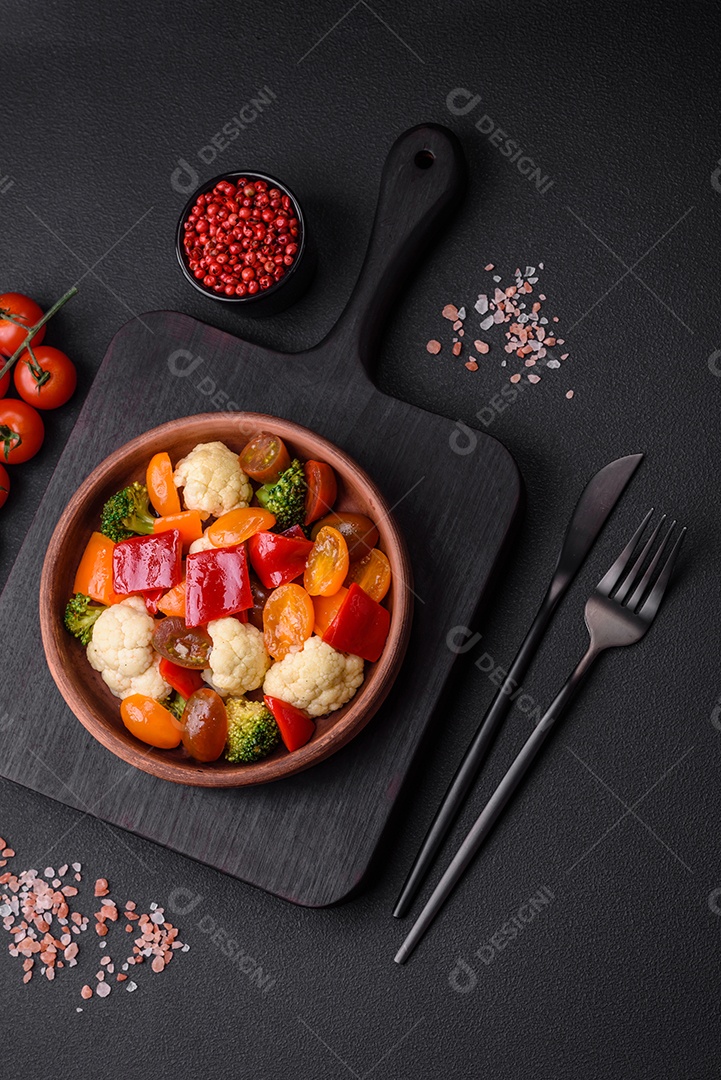 Deliciosa salada de tomate cereja fresco, pimentão, brócolis e couve-flor com sal e especiarias sobre um fundo escuro de concreto