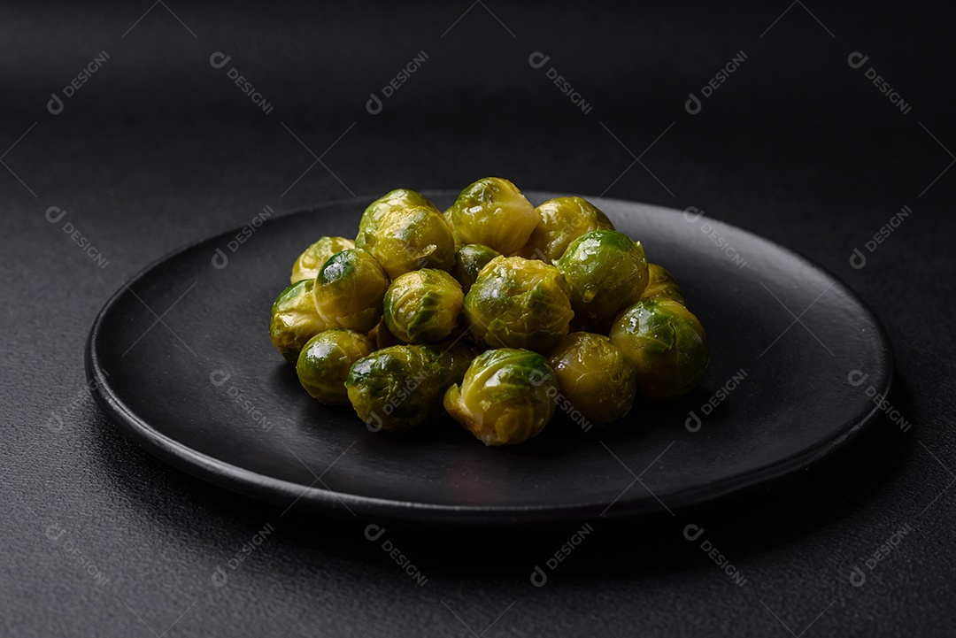 Deliciosas couves de Bruxelas cozidas em um prato de cerâmica sobre um fundo escuro de concreto. Comida vegetariana