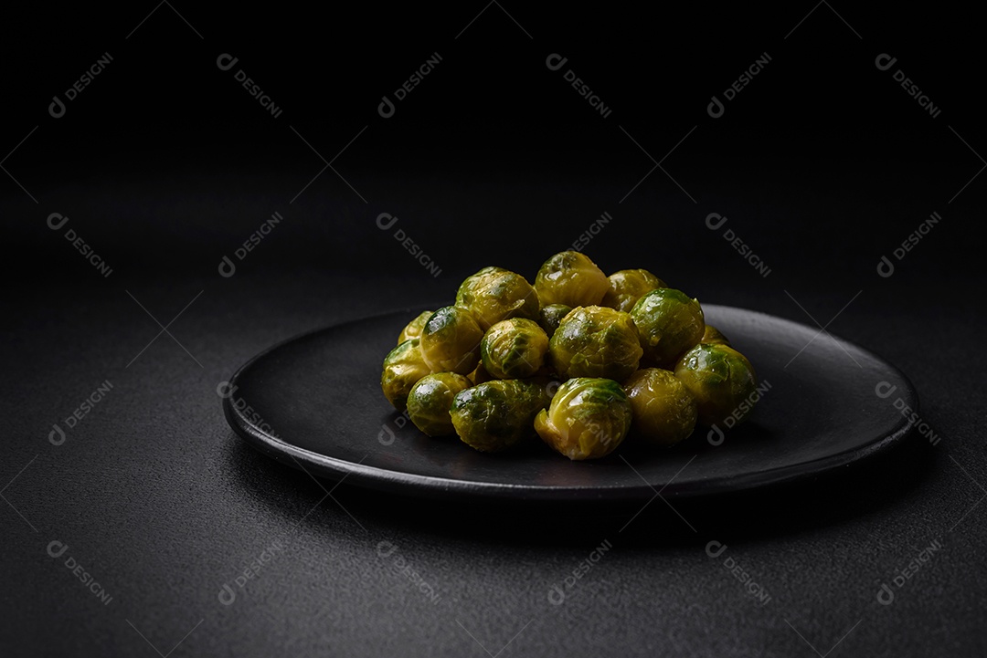 Deliciosas couves de Bruxelas cozidas em um prato de cerâmica sobre um fundo escuro de concreto. Comida vegetariana
