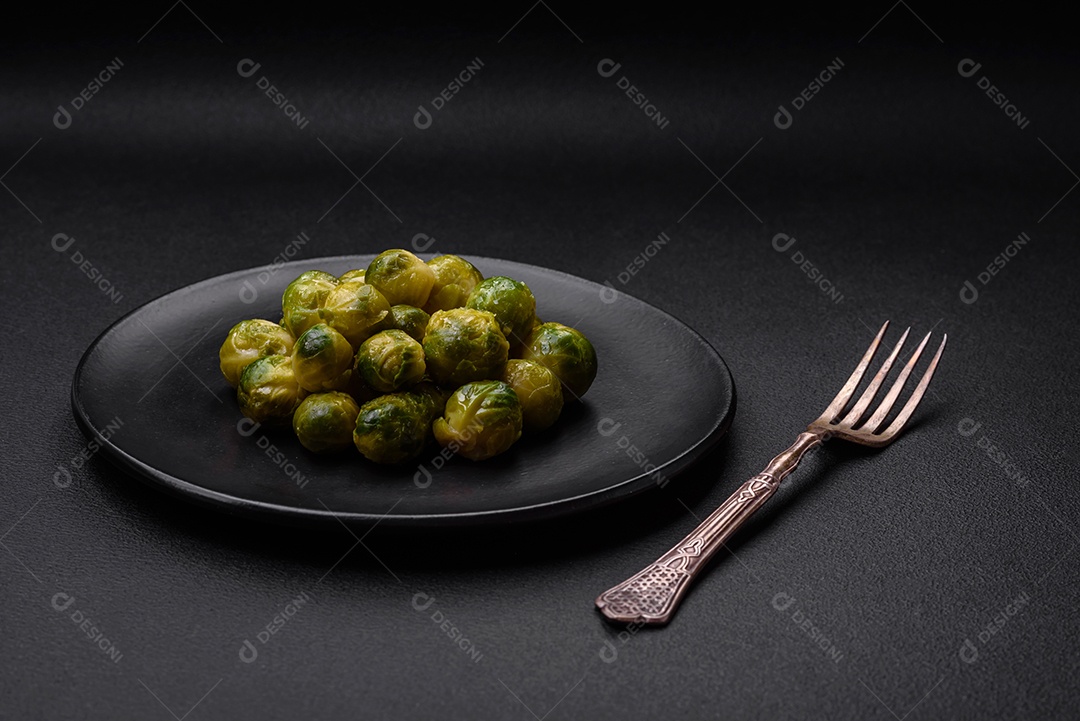 Deliciosas couves de Bruxelas cozidas em um prato de cerâmica sobre um fundo escuro de concreto. Comida vegetariana