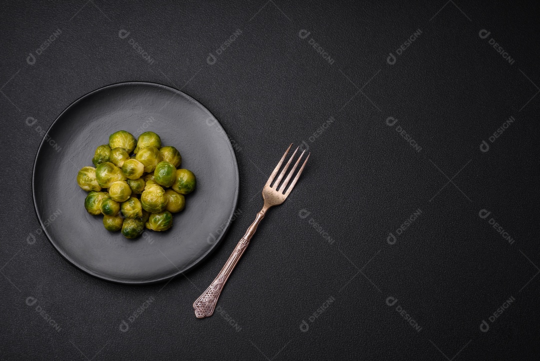 Deliciosas couves de Bruxelas cozidas em um prato de cerâmica sobre um fundo escuro de concreto. Comida vegetariana