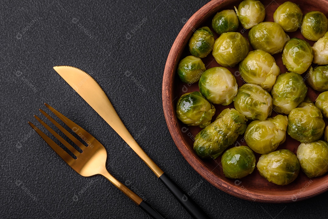 Deliciosas couves de Bruxelas cozidas em um prato de cerâmica sobre um fundo escuro de concreto. Comida vegetariana