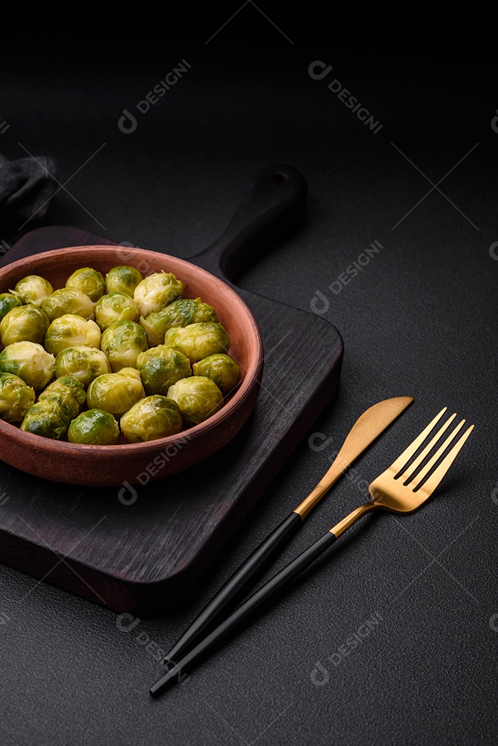 Deliciosas couves de Bruxelas cozidas em um prato de cerâmica sobre um fundo escuro de concreto. Comida vegetariana
