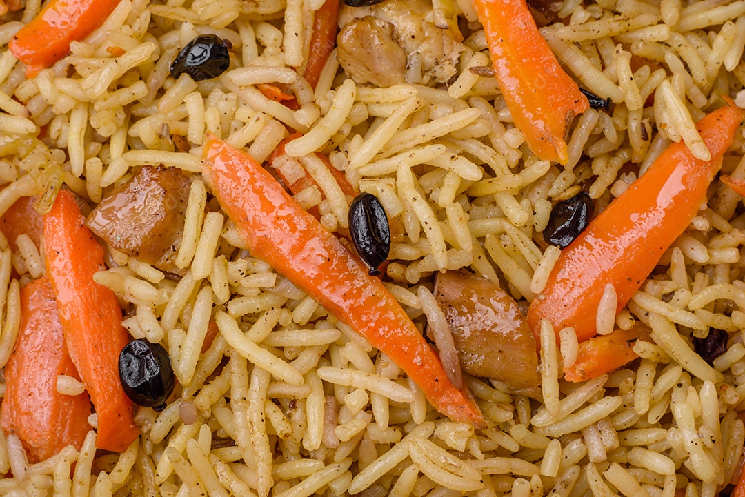 Delicioso pilaf uzbeque com frango, cenoura, bérberis, especiarias e ervas sobre um fundo escuro de concreto