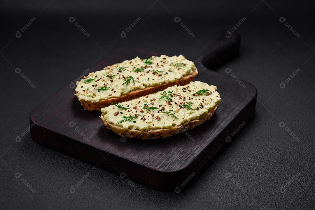 Torradas grelhadas com pasta de abacate, ovos, cream cheese, sal, especiarias e ervas sobre uma mesa de concreto texturizado
