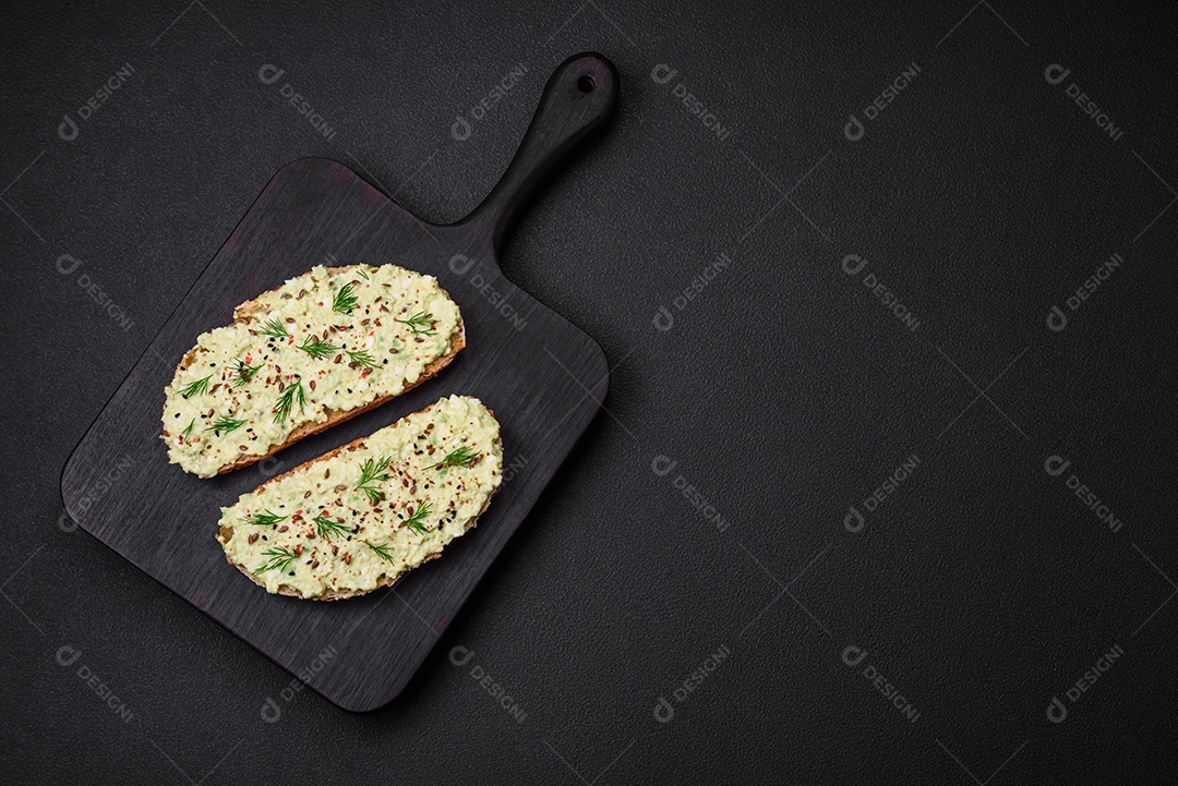 Torradas grelhadas com pasta de abacate, ovos, cream cheese, sal, especiarias e ervas sobre uma mesa de concreto texturizado