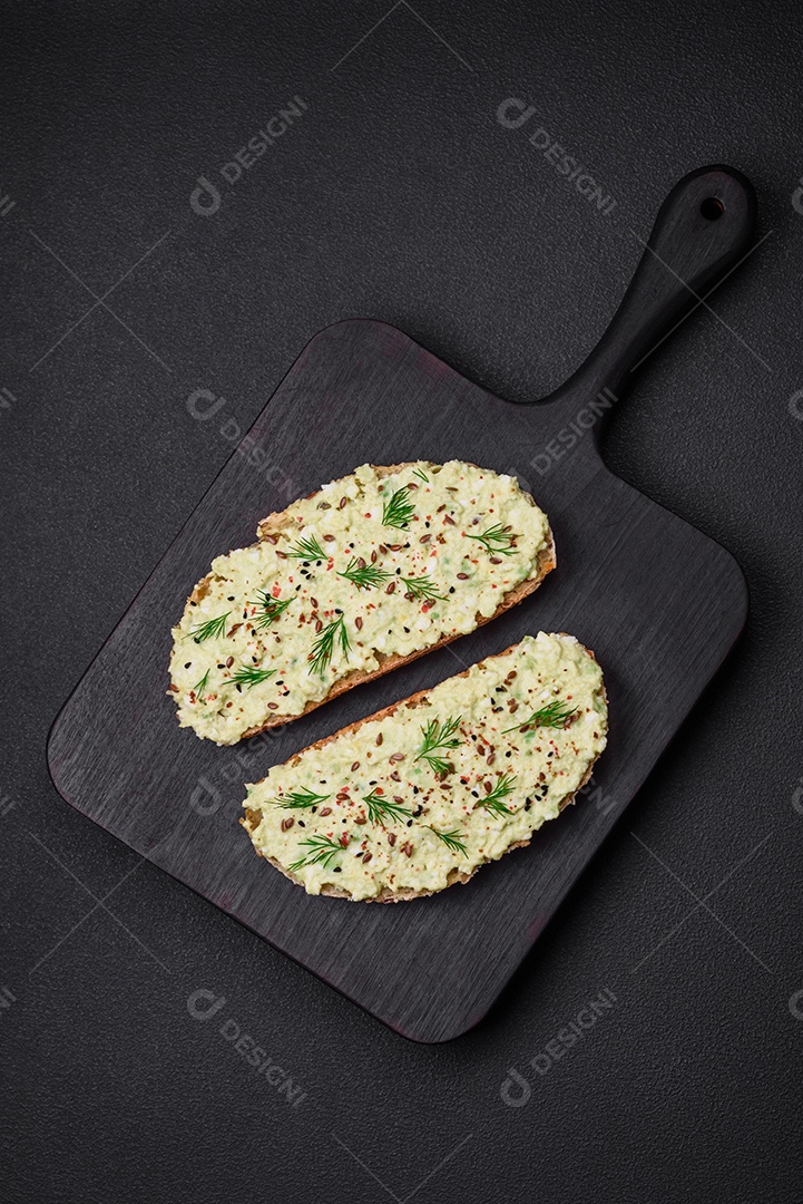 Torradas grelhadas com pasta de abacate, ovos, cream cheese, sal, especiarias e ervas sobre uma mesa de concreto texturizado