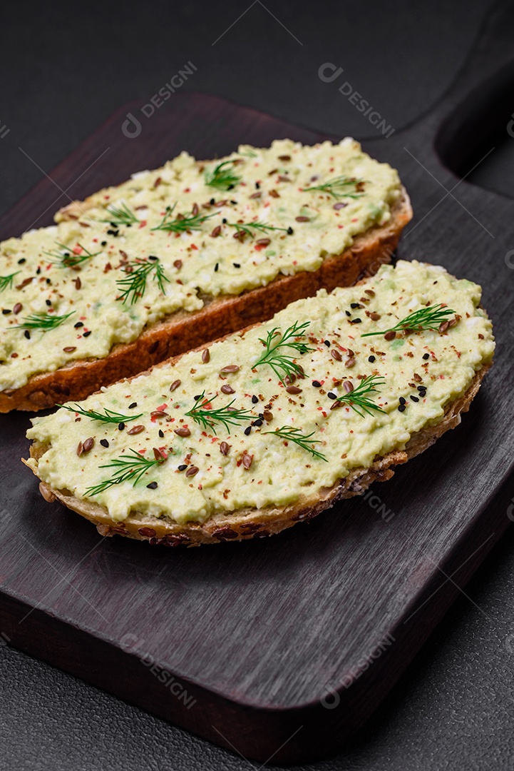 Torradas grelhadas com pasta de abacate, ovos, cream cheese, sal, especiarias e ervas sobre uma mesa de concreto texturizado
