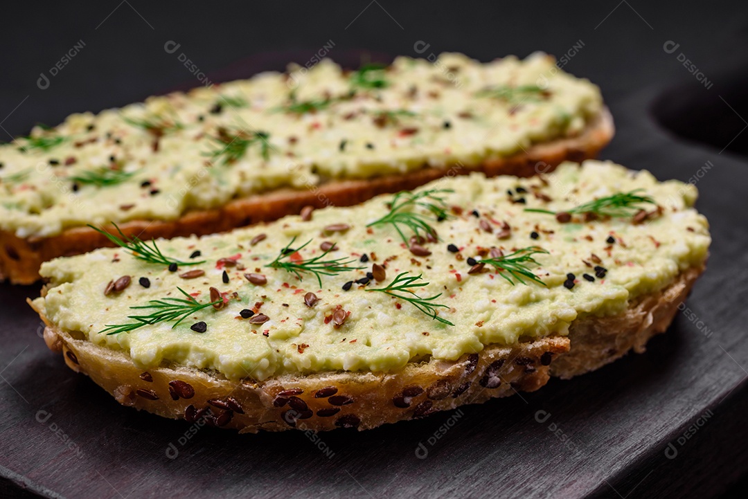 Torradas grelhadas com pasta de abacate, ovos, cream cheese, sal, especiarias e ervas sobre uma mesa de concreto texturizado