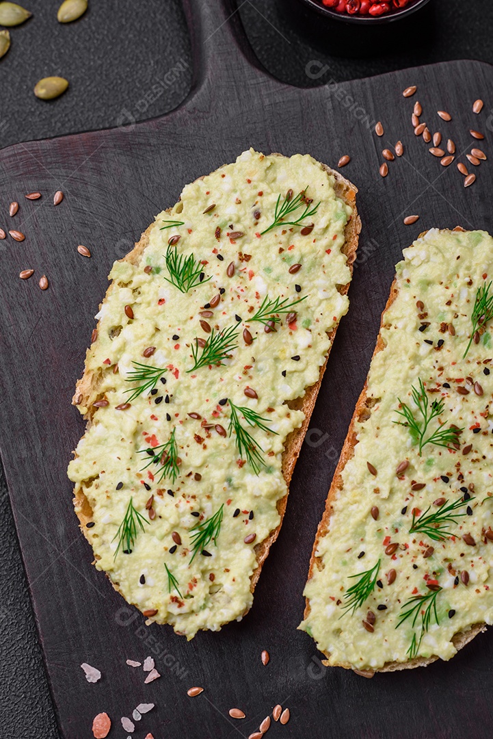 Torradas grelhadas com pasta de abacate, ovos, cream cheese, sal, especiarias e ervas sobre uma mesa de concreto texturizado