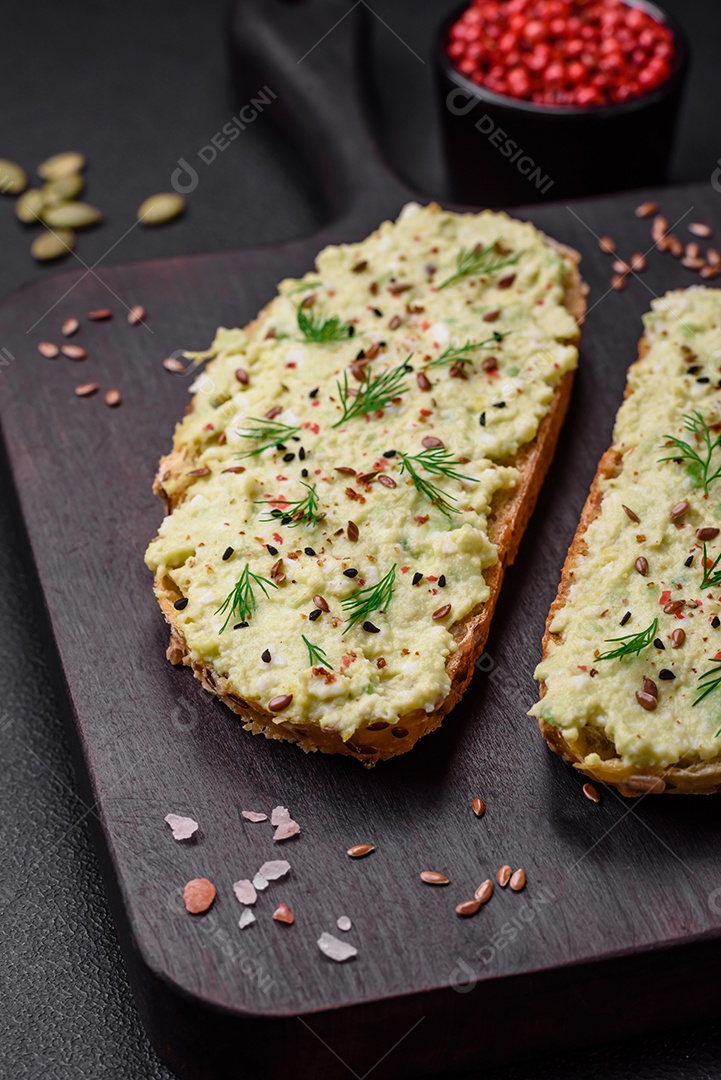Torradas grelhadas com pasta de abacate, ovos, cream cheese, sal, especiarias e ervas sobre uma mesa de concreto texturizado
