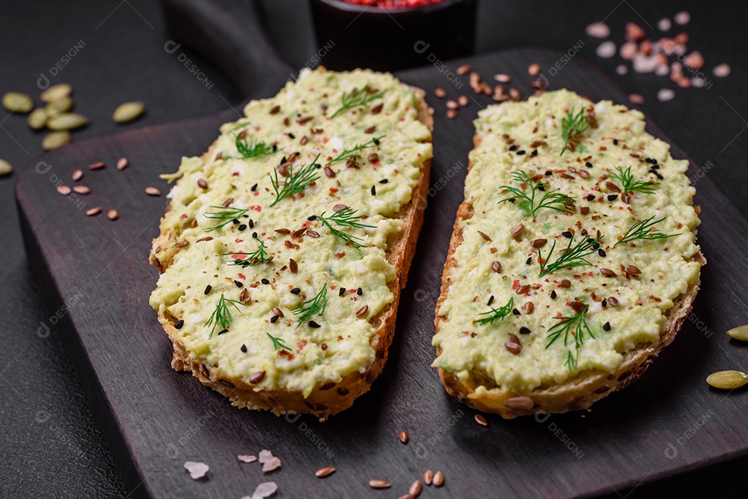 Torradas grelhadas com pasta de abacate, ovos, cream cheese, sal, especiarias e ervas sobre uma mesa de concreto texturizado