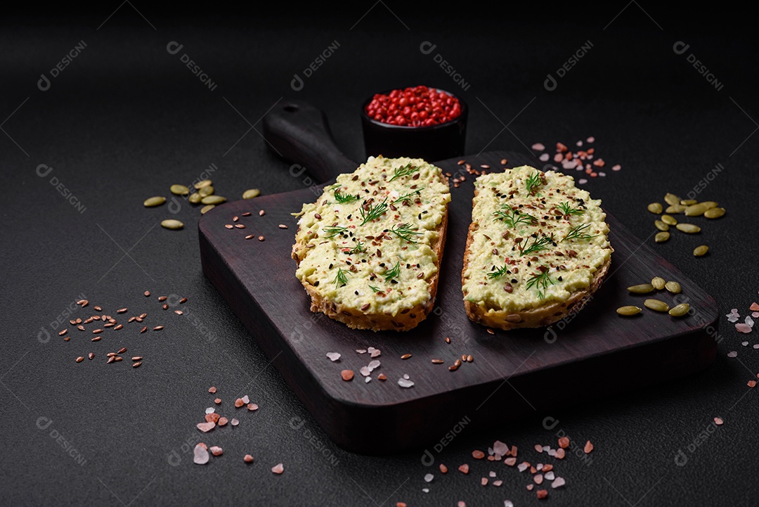 Torradas grelhadas com pasta de abacate, ovos, cream cheese, sal, especiarias e ervas sobre uma mesa de concreto texturizado