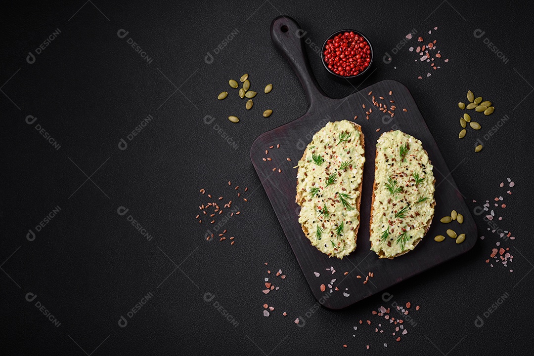Torradas grelhadas com pasta de abacate, ovos, cream cheese, sal, especiarias e ervas sobre uma mesa de concreto texturizado